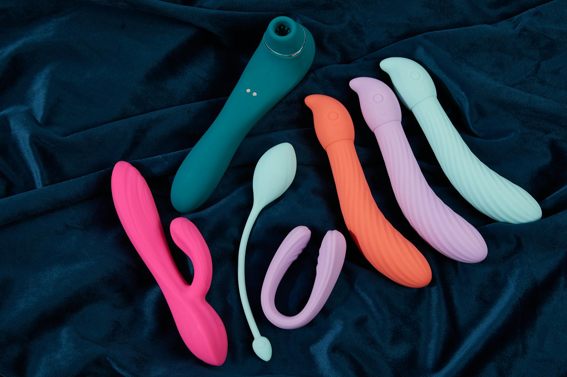 Vibrant display of silicone sex toys on dark blue fabric, showcasing various shapes and colors.