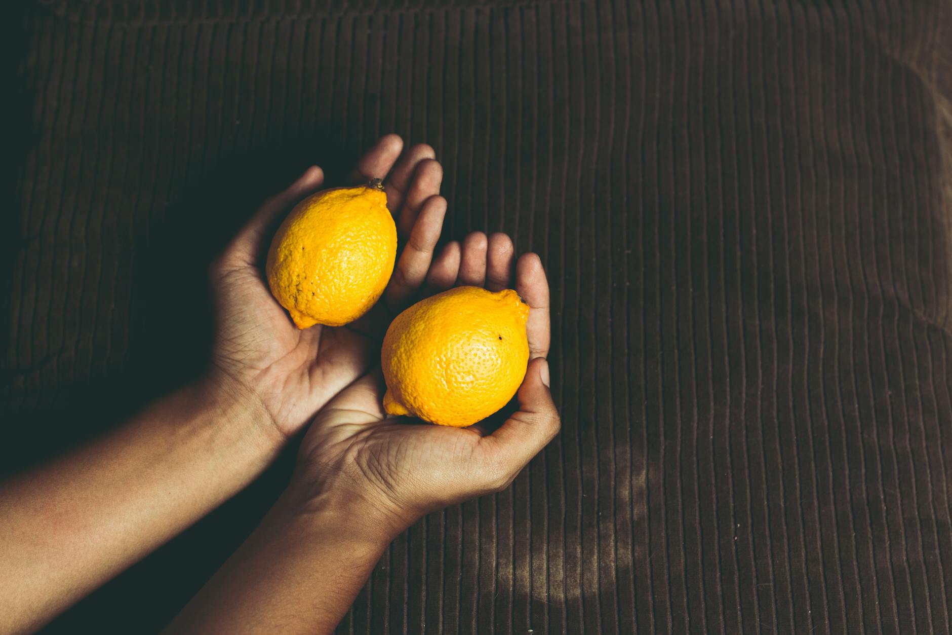 A close-up of fresh lemons held in cupped hands on a brown surface, symbolizing freshness and care.