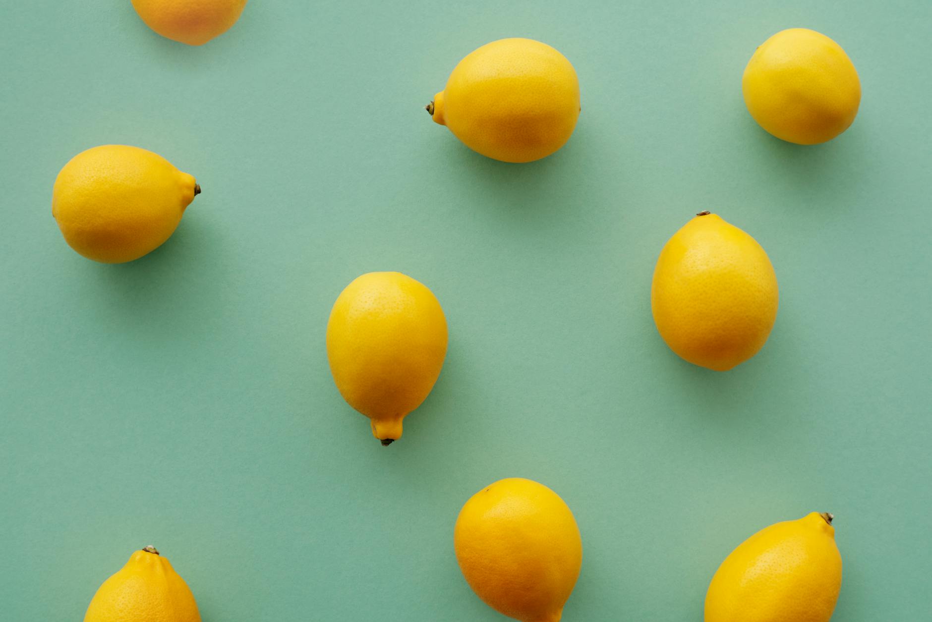 Limones amarillo brillante dispuestos sobre fondo verde pastel, creando una composición vibrante y fresca