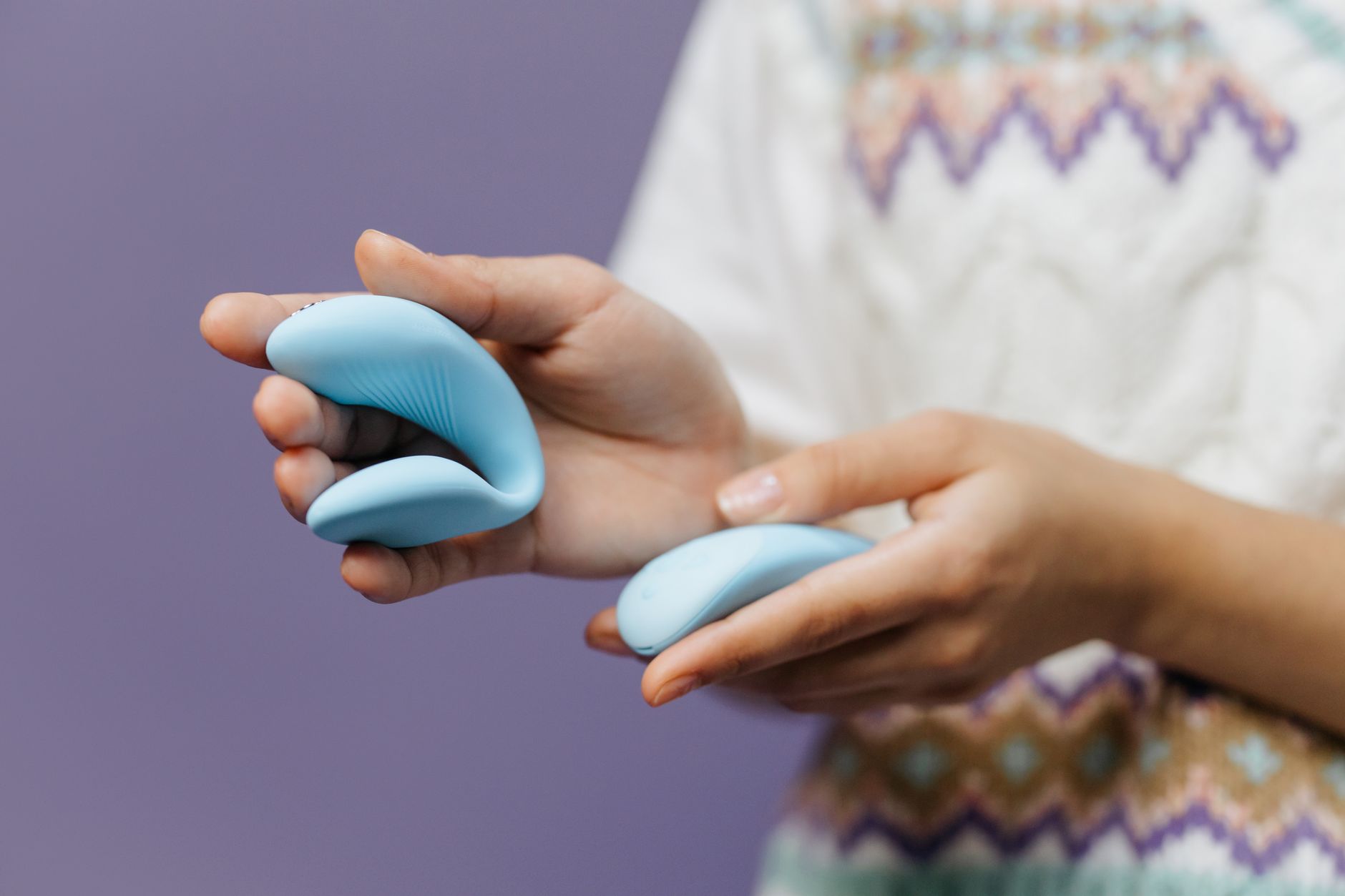 Primer plano íntimo de manos sosteniendo un vibrador de limón elegante contra un fondo púrpura.