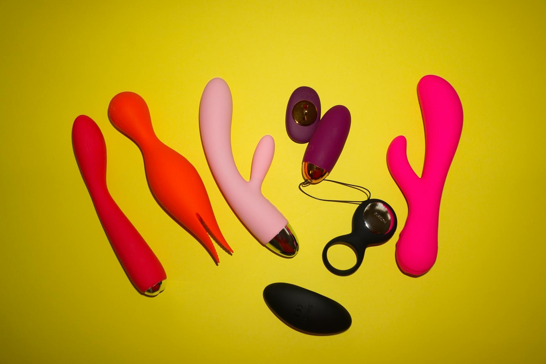 Vibrador azul rodeado de flores y rodajas de naranja sobre fondo amarillo brillante